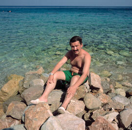 Home assegut a les roques amb la mar de fons